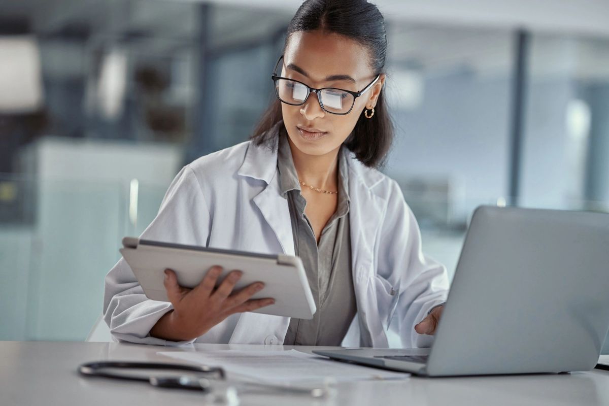 Focused clinician working across tablet and laptop