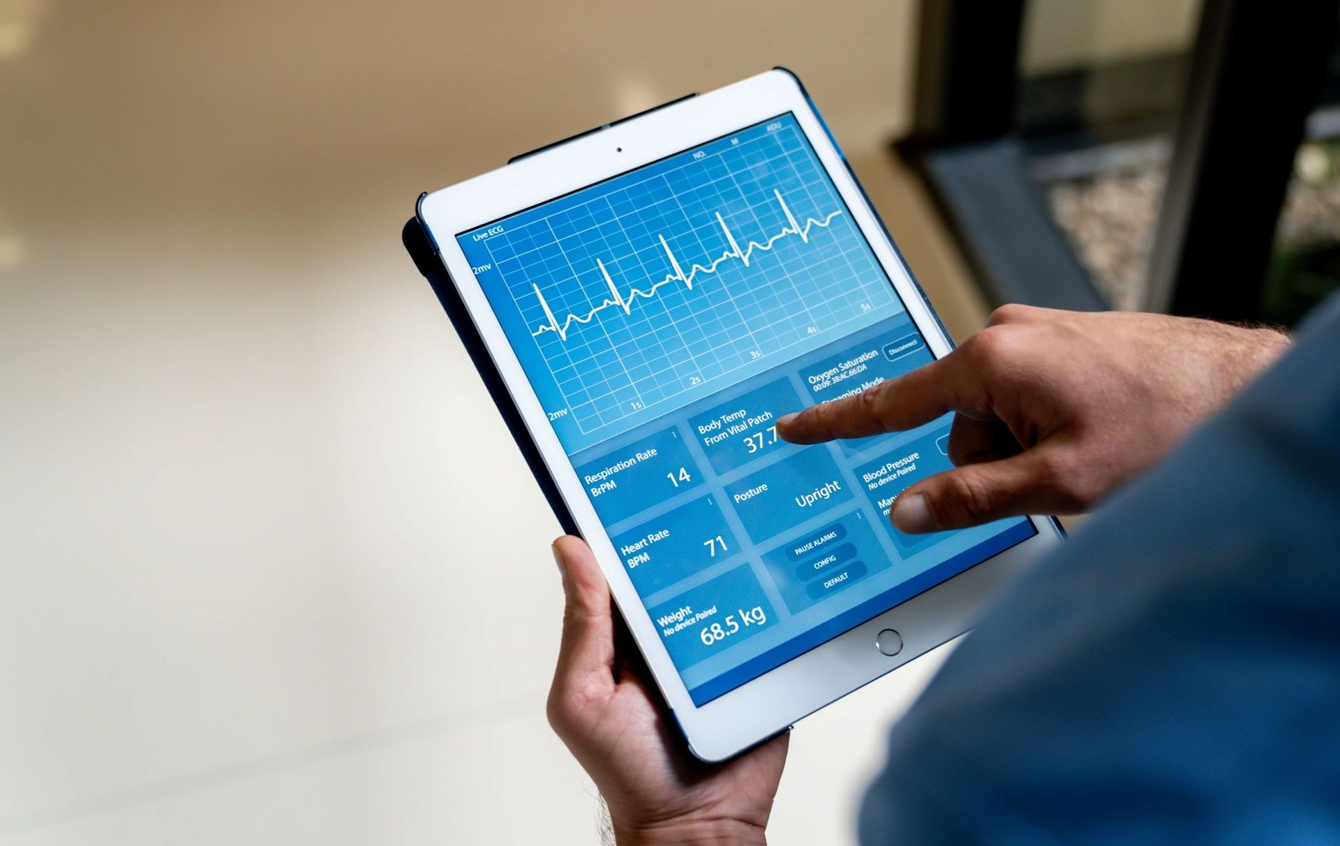 Hands holding a tablet showing live ECG trace and patient vitals